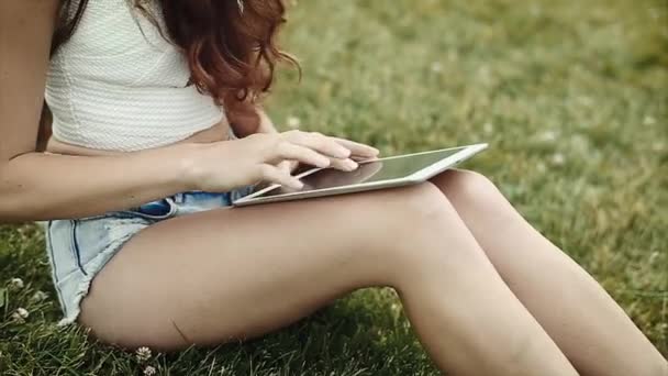 Красивая девушка с длинными кудрявыми волосами играет с устройством в руках на ногах — стоковое видео