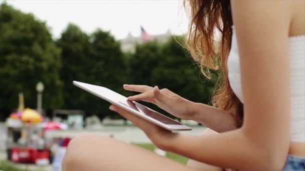 Beautiful Girl in White Shirt and Jean Shorts With Long Brown Hair is Playing on Her Device With Downtown on the Background in Slow Motion — Stock Video