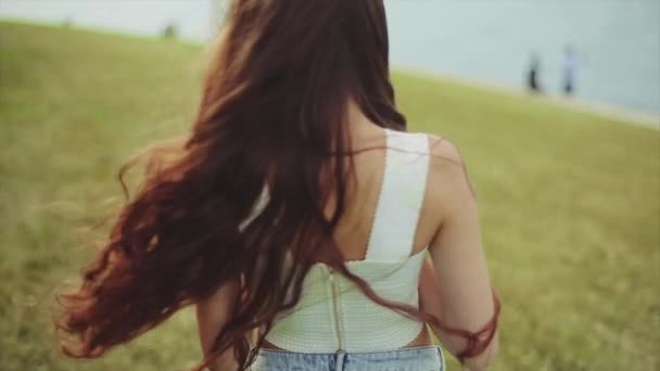 Hermosa chica con el pelo rizado marrón muy largo caminando con su computadora portátil en la parte delantera del lago y el centro de la ciudad en cámara lenta — Vídeos de Stock