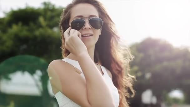 Entusiasta chica hablando por teléfono mientras los rayos del sol están brillando . — Vídeos de Stock