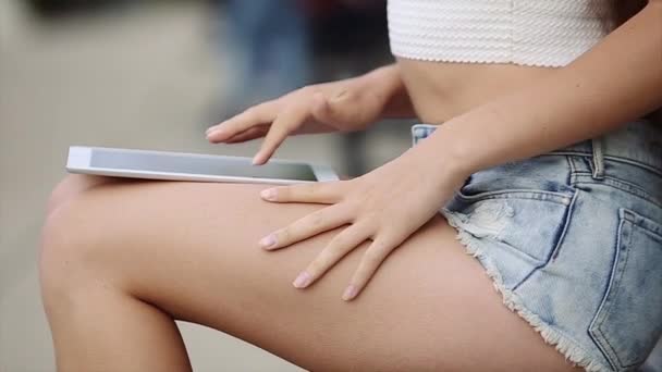 Hermosa chica de camisa blanca y gafas de sol negras está sentada en el banco y hablando por teléfono con muchas personas en segundo plano en cámara lenta — Vídeos de Stock