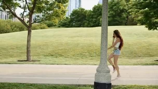 Söt flicka hoppa med sin mobiltelefon i stor grön Park med höga byggnader i bakgrunden — Stockvideo