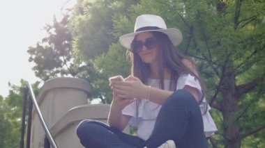 Şapkalı korkuluk Park bir ağacın altında oturup telefon, şehir merkezinde, genç güzel kadın.