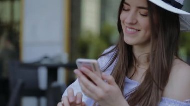 Genç, gülümseyen kadın şapkalı, telefon açık bir Cafe, bir masada oturan çağırıyor.
