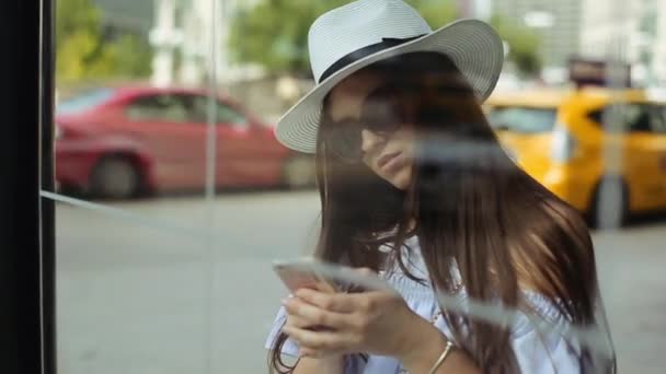 Junge attraktive Frau mit Hut telefoniert an Bushaltestelle neben Straße. — Stockvideo