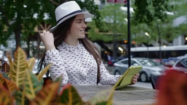 Jonge mooie lachende vrouw zitten op een stoep Cafe in het centrum van de stad, met Tablet. — Stockvideo