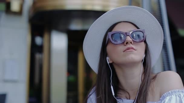 Jeune belle femme en chapeau et lunettes qui reflètent gratte-ciel Parler sur casque . — Video