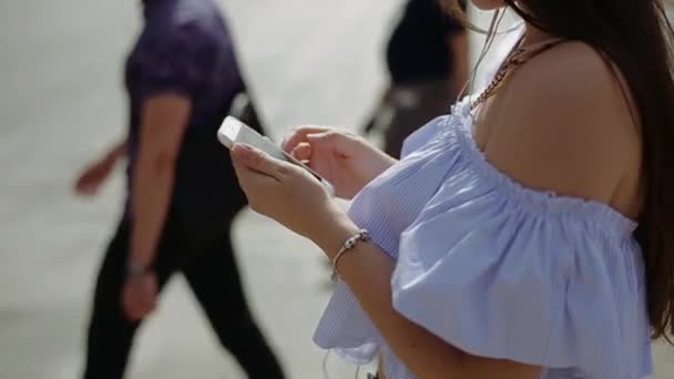 Молодая женщина в шляпе улыбается, общаясь в социальных сетях, используя смартфон в центре города на пешеходном переходе . — стоковое видео