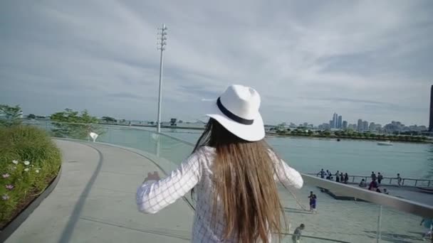 Young Woman in Hat and Glasses Dancing on Waterfront With High-Rise Slow Motion — Stock Video