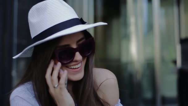 Jonge mooie lachende vrouw hoed om te praten over de telefoon op achtergrond van draaideuren. — Stockvideo