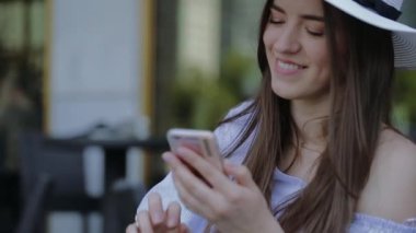 Genç, gülümseyen kadın şapkalı, telefon açık bir Cafe, bir masada oturan çağırıyor.