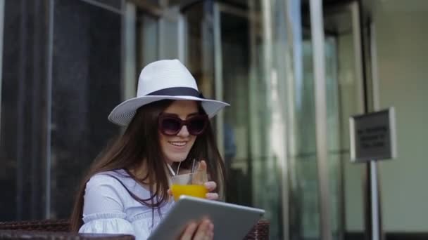 Ελκυστική γυναίκα κάθεται στο δρόμο Cafe και πίνει πορτοκάλι χυμό. — Αρχείο Βίντεο