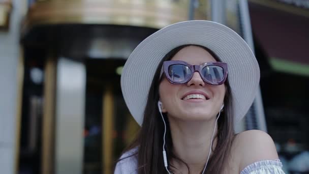 Jeune belle femme en chapeau et lunettes qui reflètent gratte-ciel Parler sur casque . — Video