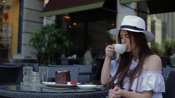 若い女性が飲むコーヒーに座って外のカフェやテラスで. — ストック動画