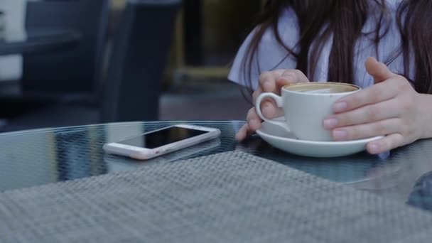 Agradável jovem mulher mantém xícara de café em suas mãos sentado no café de rua . — Vídeo de Stock