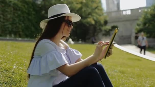 Όμορφη γυναίκα είναι εργάζονται με Tablet pc κάθεται στο γρασίδι στο πάρκο. — Αρχείο Βίντεο
