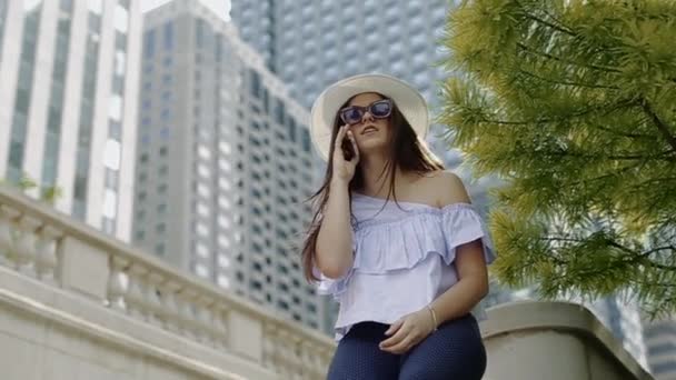 Mladá žena je povídání na mobil sedět na kamenný plot — Stock video