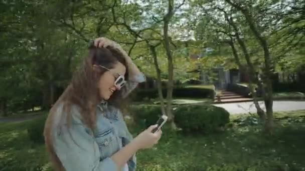 Молодая женщина набирает номер, идущий по улице в парке . — стоковое видео