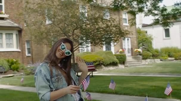 Mujer sacude su mano y mantiene pequeña bandera americana en su brazo derecho . — Vídeos de Stock