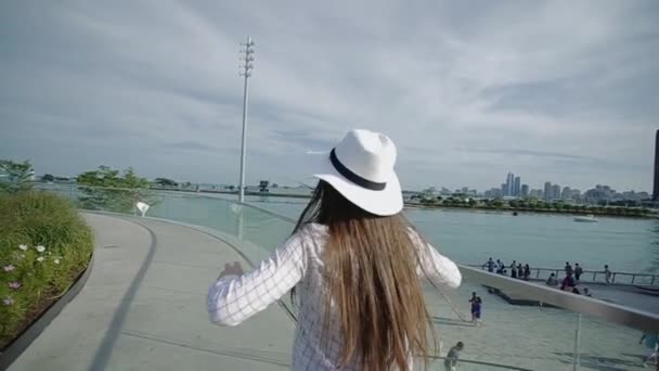 Mujer joven con sombrero y gafas bailando en el paseo marítimo con movimiento lento de gran altura — Vídeos de Stock
