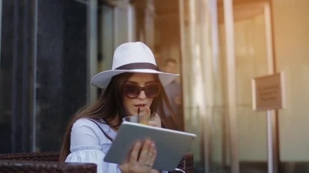 Mulher atraente senta-se no café de rua e bebe suco de laranja . — Vídeo de Stock