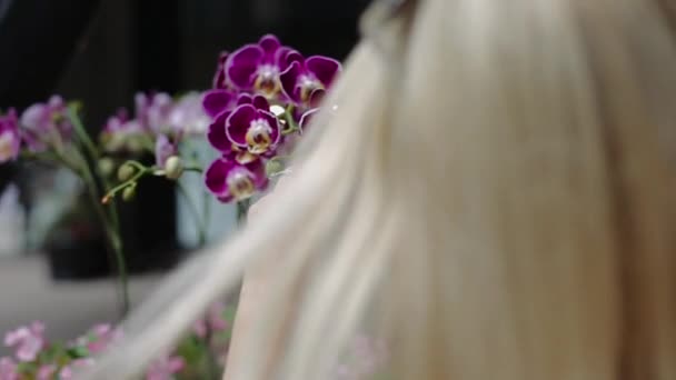 Joven atractiva rubia chica fotografiada en un teléfono móvil púrpura orquídea flor . — Vídeo de stock