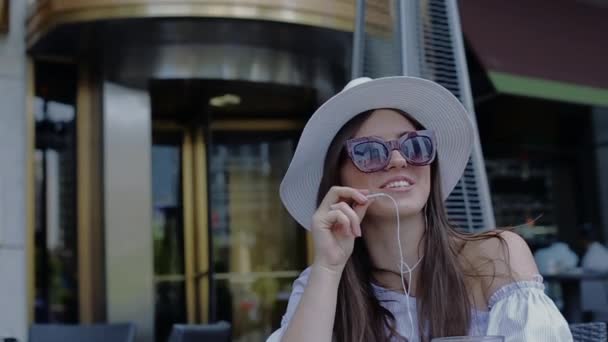 Belle jeune femme parle au téléphone souriant assis dans le café à l'extérieur . — Video