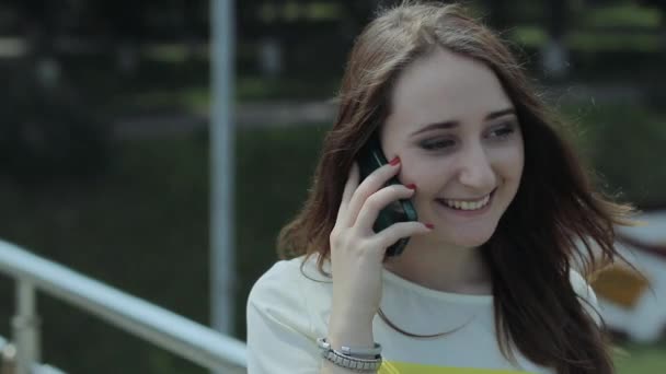 Młoda dziewczyna stoi na podwórku tarcze Bridge, radośnie rozmawia przez telefon komórkowy. — Wideo stockowe
