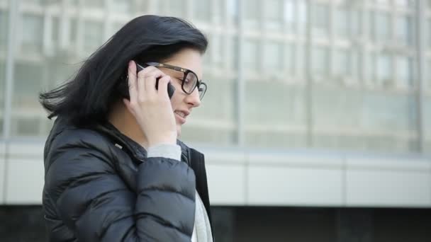 Дівчина в окулярах говорить по телефону. Дівчина в чорній куртці — стокове відео