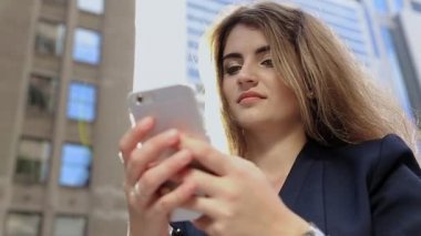 bir genç kız sokakta, ayakta bir çağrı alır ve konuşurken, gülümseyen.