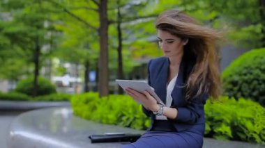 Kaldırımda Oturan Bir Tablet Üzerinde Çalışan Genç Bir Kız, ve Gülümsüyor. Sırada Çanta var..