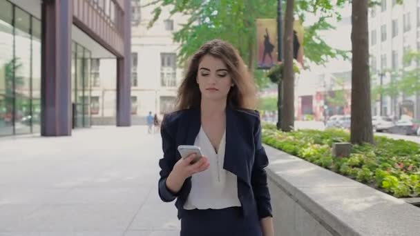 Joven chica de negocios caminando por la calle, sonriendo y hablando por teléfono . — Vídeos de Stock