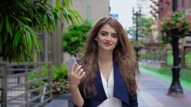 Uma menina vai para baixo da avenida, onde as plantas crescem, e falando ao telefone . — Vídeo de Stock