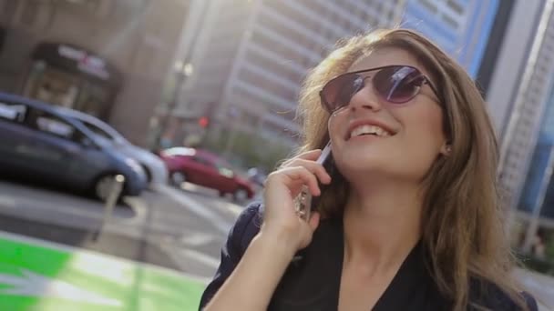Młoda dziewczyna w okulary stojące obok drogi z samochodami i rozmawiać przez telefon. Śmiech, radość. — Wideo stockowe
