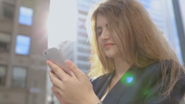 Uma jovem está perto de casas e mostradores em um telefone móvel, falando . — Vídeo de Stock