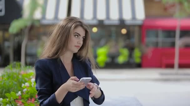 Uma menina fica na praça perto dos canteiros e Nervoso olha para o seu relógio e telefone . — Vídeo de Stock