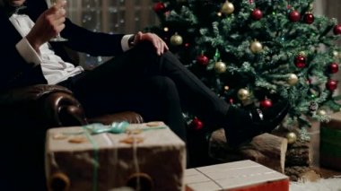 Noel ağacı ve zam bir kadeh şampanya yanında bir sandalyede oturan bir genç adam.