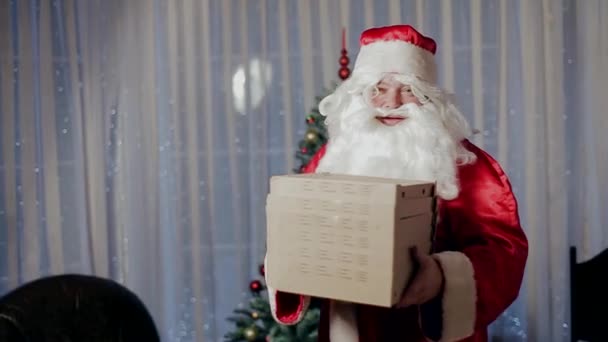 Weihnachtsmann in der Nähe des Weihnachtsbaums mit einer Schachtel mit einer Überraschung. — Stockvideo