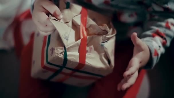 Manos de niño pequeño tratando de abrir un regalo, envuelto con papel . — Vídeos de Stock