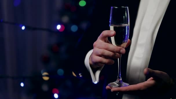 Een glas Champagne in de handen van een Man op een achtergrond versierd kerstboom. — Stockvideo