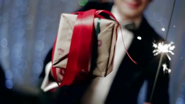 Egy fiatal férfi, egy ajándék és a csillagszóró karácsonyfa előtt. — Stock videók