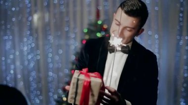 Genç adam bir şekilde dekore edilmiş Noel ağacı önünde mevcut ve tutan maytap inceliyor.