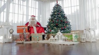 Kırmızı kostümlü Noel Baba Noel ağacı bir tablo tutarak yakın oturur adam
