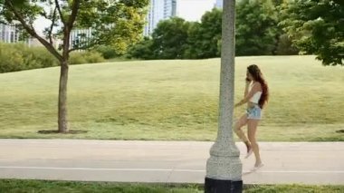 Güzel kız büyük yeşil park cep telefonunu uzun binalar içinde belgili tanımlık geçmiş ile atlama