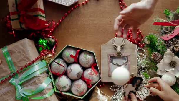 Algunas personas hacen juguetes de Año Nuevo en una caja en una mesa donde un montón de decoraciones de Navidad . — Vídeos de Stock