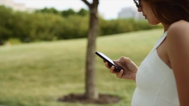 Petite meisje in een wit overhemd en een zwarte zonnebril overslaan met haar telefoon en lachend. een mooi meisje praten aan de telefoon — Stockvideo