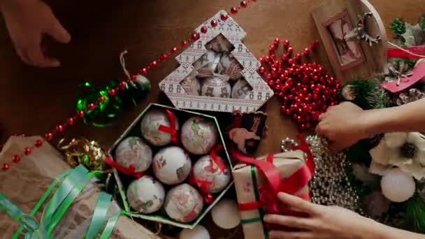Algunas manos de la gente embalaron regalos de Navidad en una mesa donde una gran cantidad de accesorios de Navidad . — Vídeos de Stock