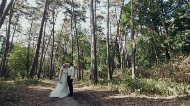 Damat ve gelin ormanın arka planında öpüşüyor.