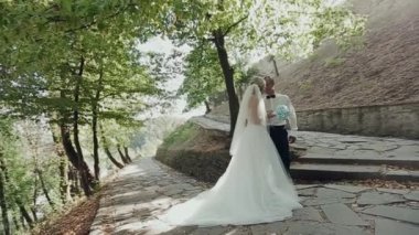 Damat ve gelin ormanın arka planında öpüşüyor.