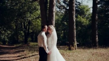 Damat ve gelin ormanın arka planında öpüşüyor.